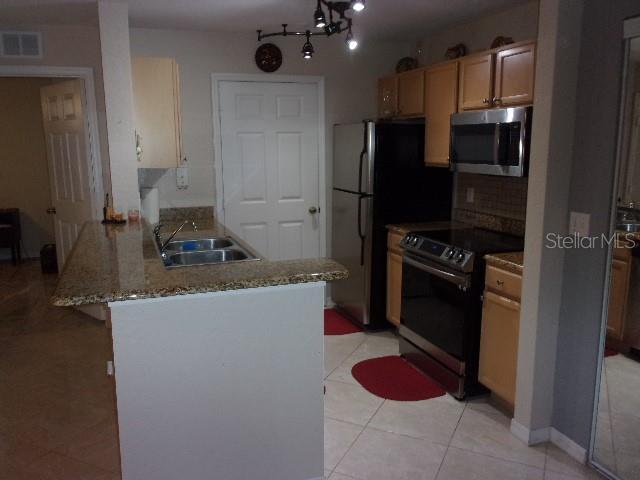 kitchen with light tile patterned floors, kitchen peninsula, appliances with stainless steel finishes, a breakfast bar, and sink