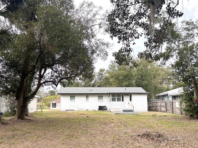 rear view of property featuring central air condition unit and a lawn