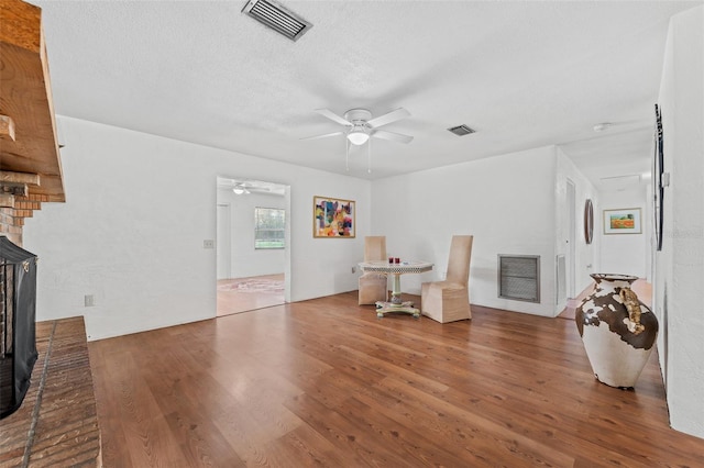 living area with ceiling fan, a fireplace, a textured ceiling, and hardwood / wood-style flooring