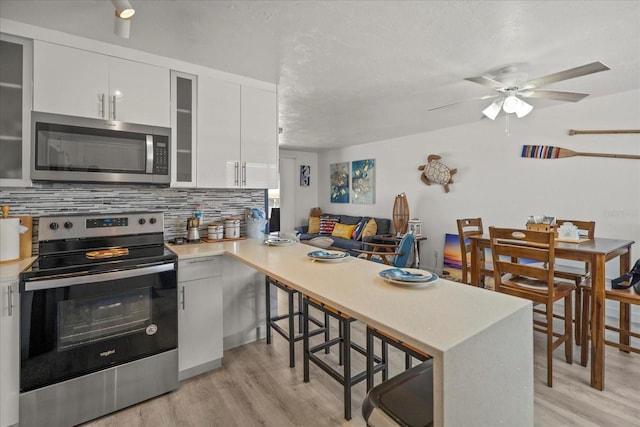 kitchen featuring backsplash, kitchen peninsula, white cabinets, and stainless steel appliances