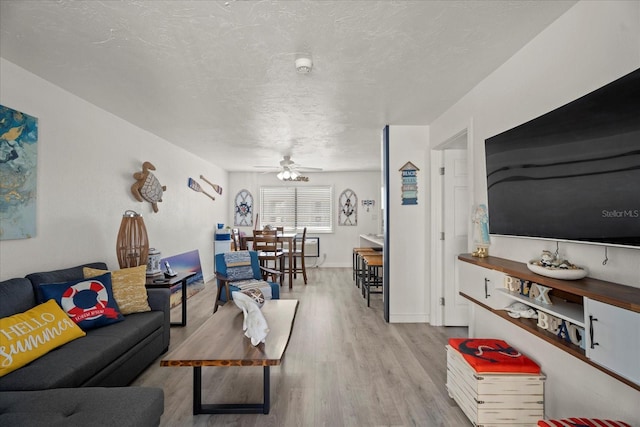 living room featuring light wood-type flooring, ceiling fan, and a textured ceiling