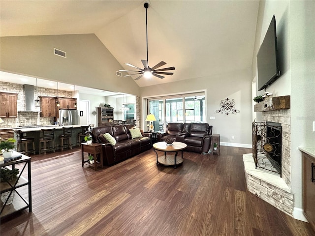 living room with ceiling fan, dark wood-type flooring, a stone fireplace, and high vaulted ceiling