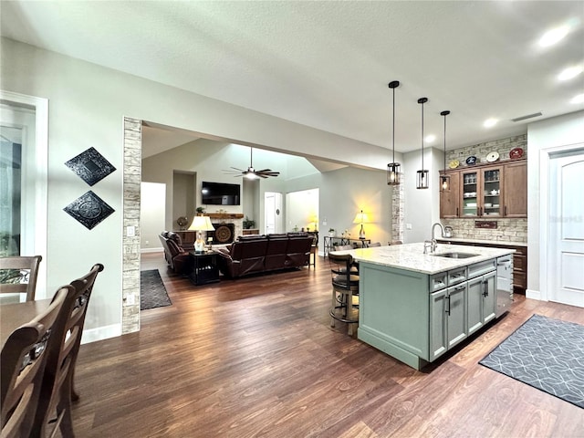 kitchen featuring sink, light stone counters, a kitchen island with sink, dark hardwood / wood-style floors, and pendant lighting