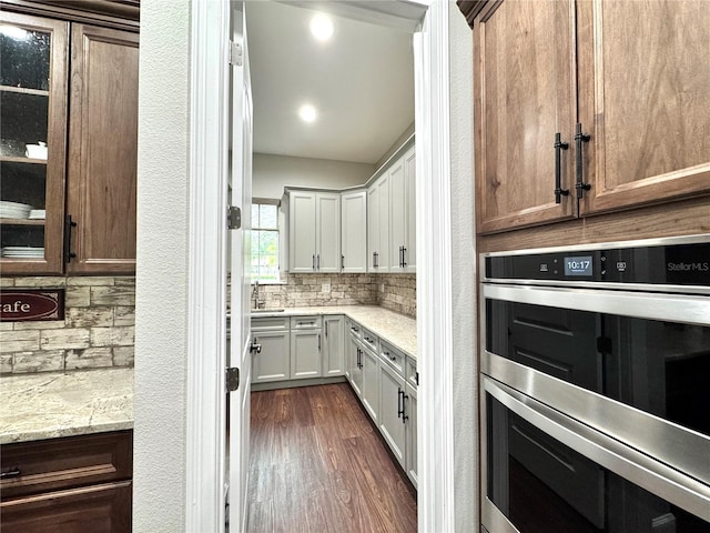 kitchen featuring double oven, white cabinetry, backsplash, and light stone countertops