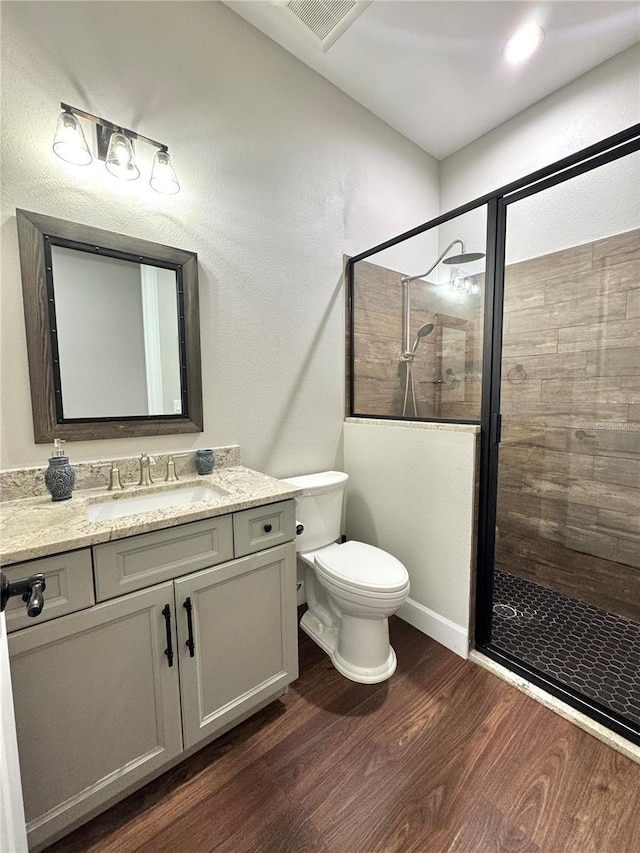 bathroom with a tile shower, vanity, toilet, and hardwood / wood-style floors