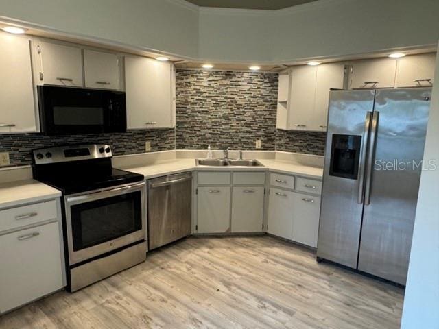 kitchen with stainless steel appliances, decorative backsplash, light wood-type flooring, white cabinetry, and sink