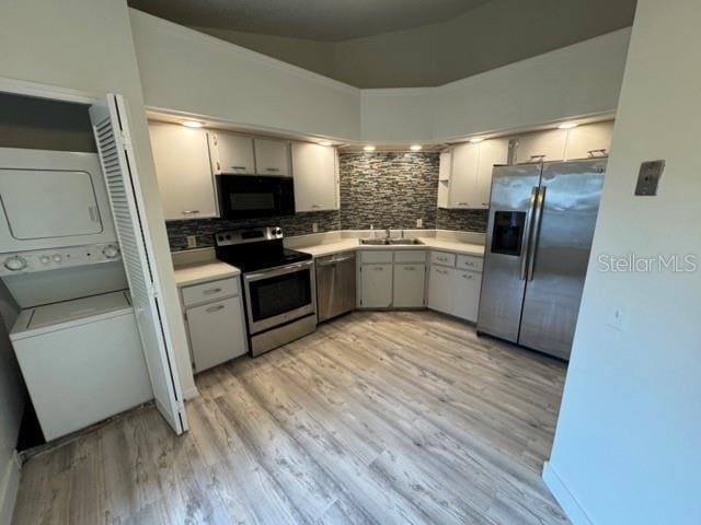 kitchen featuring stacked washing maching and dryer, vaulted ceiling, light hardwood / wood-style floors, tasteful backsplash, and appliances with stainless steel finishes