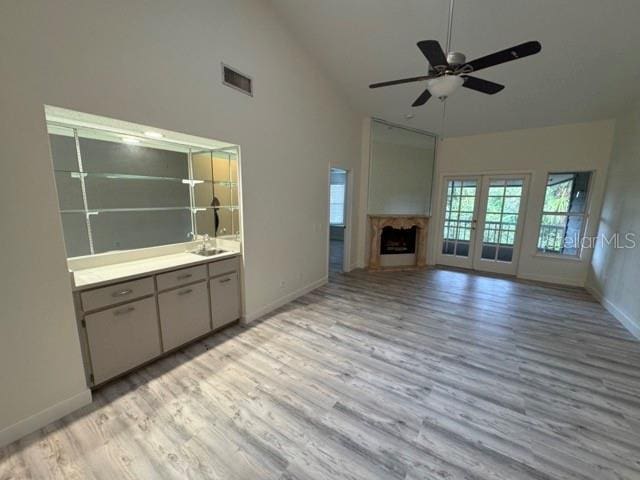 unfurnished living room featuring french doors, light hardwood / wood-style floors, high vaulted ceiling, ceiling fan, and sink