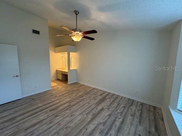 unfurnished living room with ceiling fan, vaulted ceiling, a textured ceiling, and wood-type flooring