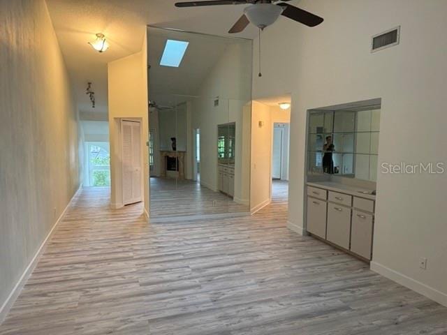 hallway with light hardwood / wood-style flooring, a skylight, and high vaulted ceiling