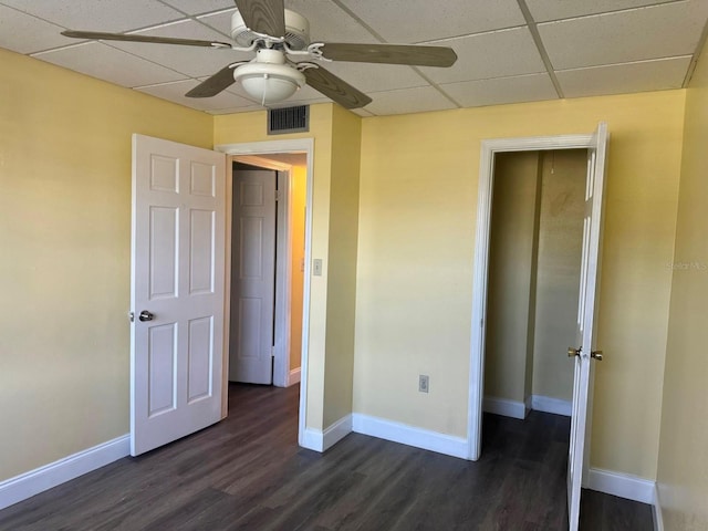 unfurnished bedroom with ceiling fan, dark wood-type flooring, and a drop ceiling