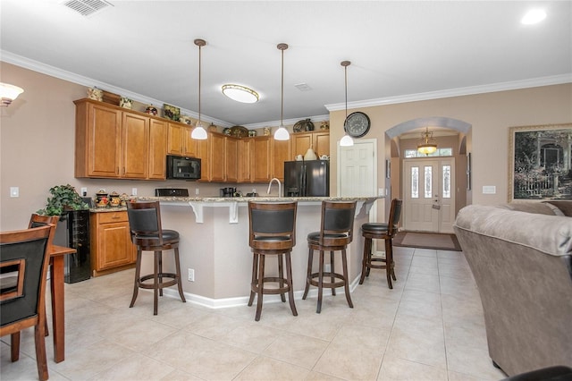 kitchen featuring black appliances, a breakfast bar, decorative light fixtures, and an island with sink