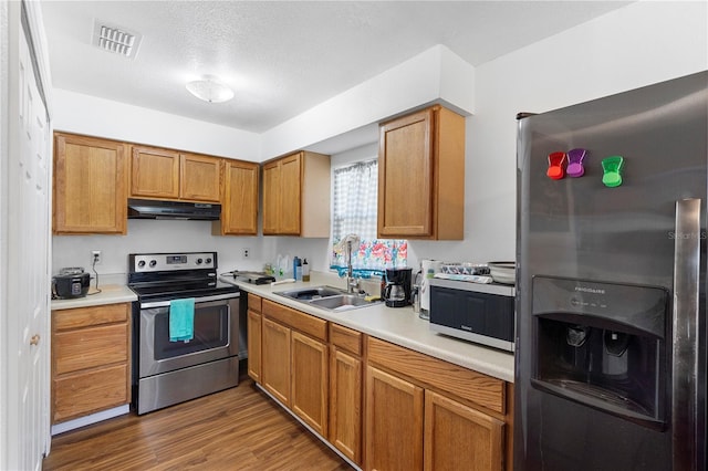 kitchen with appliances with stainless steel finishes, sink, hardwood / wood-style floors, and a textured ceiling