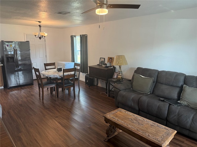 living room featuring dark wood-type flooring, ceiling fan with notable chandelier, and a textured ceiling