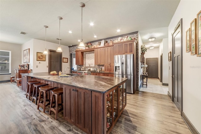 kitchen featuring hanging light fixtures, stainless steel refrigerator with ice dispenser, a kitchen breakfast bar, and a large island