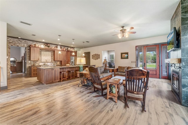 living room with ceiling fan, light wood-type flooring, and a tile fireplace