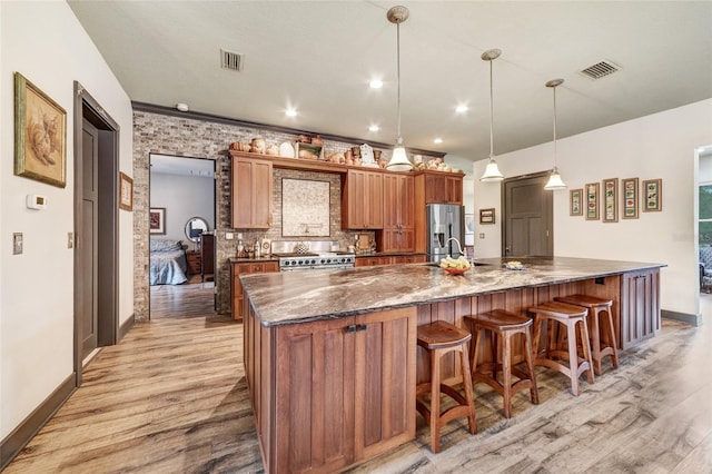 kitchen featuring pendant lighting, a kitchen bar, light wood-type flooring, stainless steel appliances, and dark stone counters