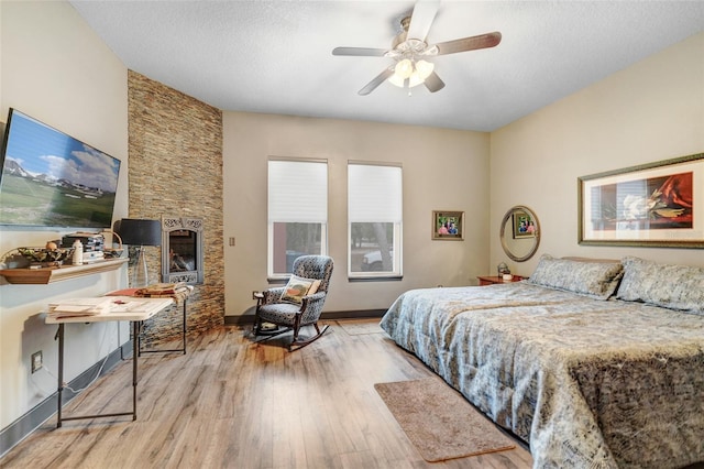 bedroom with ceiling fan, a textured ceiling, light hardwood / wood-style flooring, and a fireplace