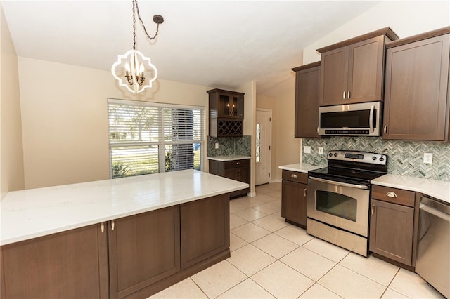 kitchen featuring light tile patterned flooring, lofted ceiling, dark brown cabinetry, hanging light fixtures, and stainless steel appliances