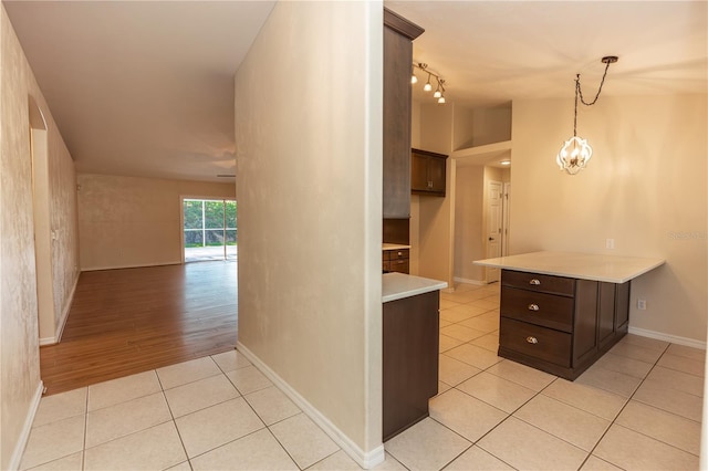 kitchen featuring vaulted ceiling, decorative light fixtures, light tile patterned floors, kitchen peninsula, and dark brown cabinets