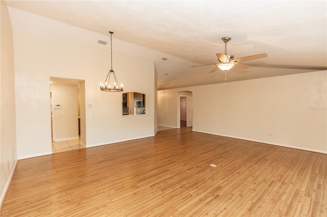 spare room featuring ceiling fan with notable chandelier, vaulted ceiling, and light hardwood / wood-style floors