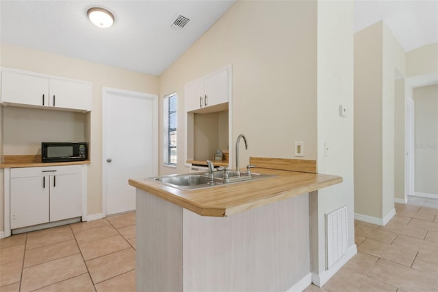 kitchen featuring light tile patterned flooring, lofted ceiling, white cabinets, and kitchen peninsula