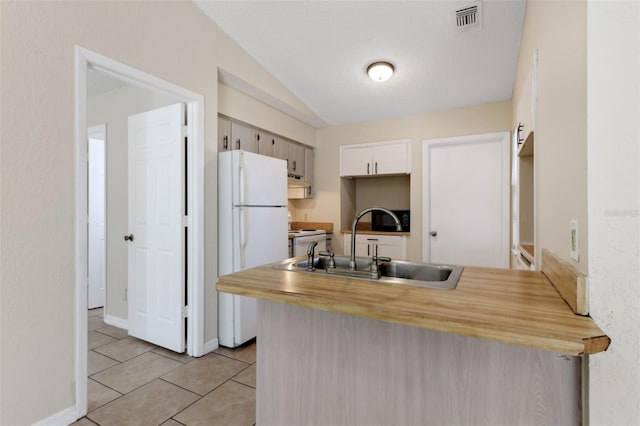 kitchen with light tile patterned flooring, lofted ceiling, sink, white refrigerator, and kitchen peninsula