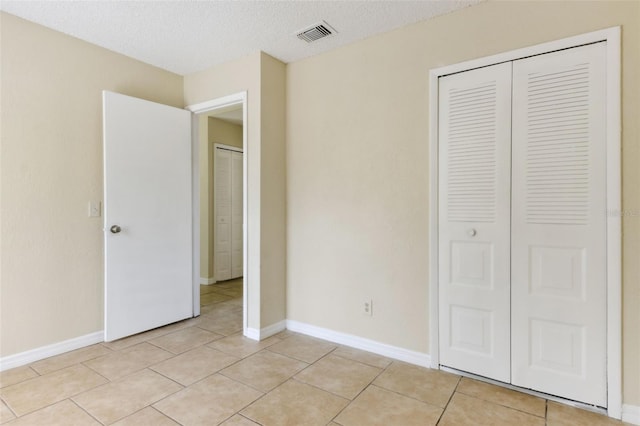 unfurnished bedroom featuring a textured ceiling, a closet, and light tile patterned floors