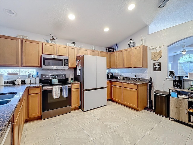 kitchen featuring stone countertops, vaulted ceiling, ceiling fan, stainless steel appliances, and backsplash