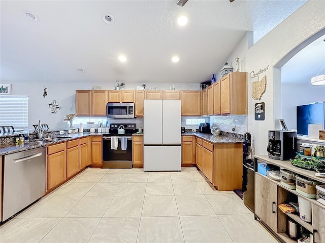 kitchen with stainless steel appliances, tasteful backsplash, light tile patterned floors, and dark stone counters