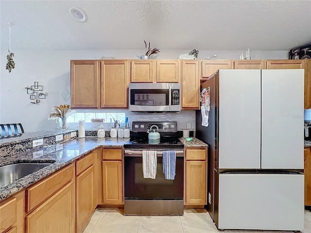 kitchen with sink, dark stone countertops, stainless steel appliances, a textured ceiling, and light tile patterned flooring