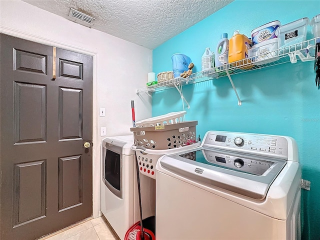 clothes washing area with separate washer and dryer, light tile patterned floors, and a textured ceiling