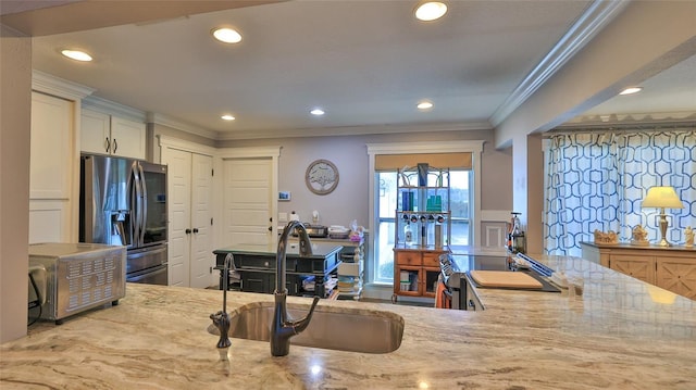 kitchen with sink, stainless steel fridge, ornamental molding, range, and light stone counters