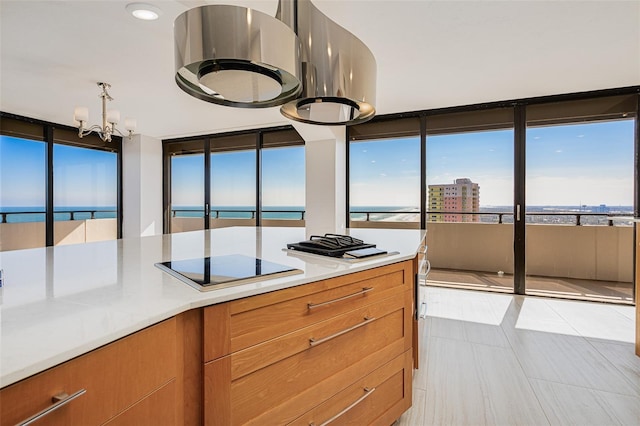 kitchen with a water view, light tile patterned flooring, an inviting chandelier, and black electric stovetop