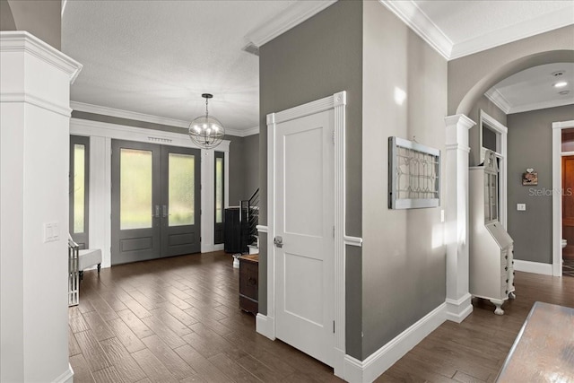 foyer featuring dark wood-type flooring, french doors, ornamental molding, and a chandelier