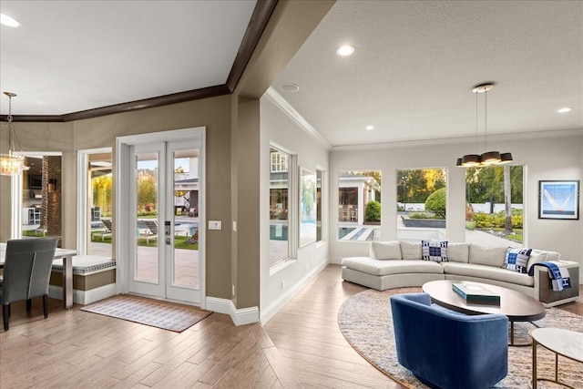 living room featuring a textured ceiling, a notable chandelier, ornamental molding, and light hardwood / wood-style flooring