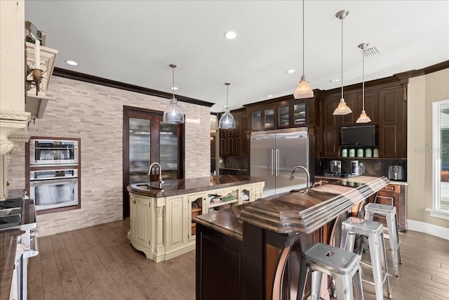 kitchen with built in fridge, hanging light fixtures, and an island with sink