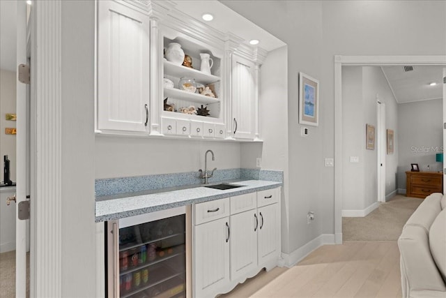 bar with light colored carpet, white cabinetry, beverage cooler, and sink