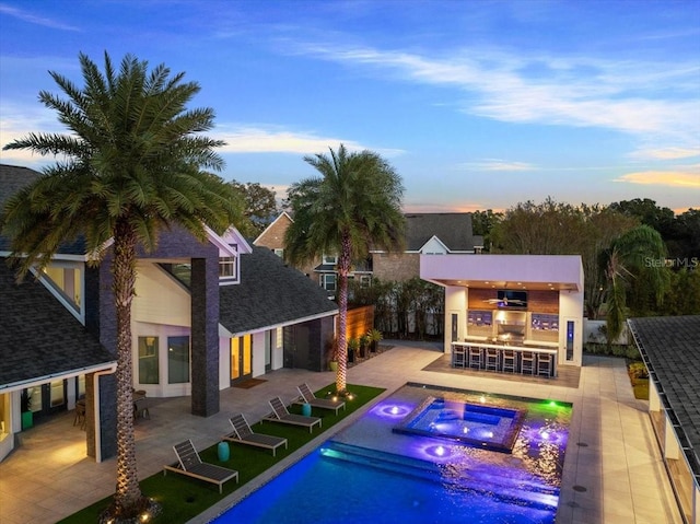 back house at dusk with a swimming pool with hot tub, an outdoor bar, and a patio