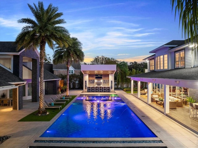 pool at dusk with an outdoor hangout area, pool water feature, a patio area, and an outdoor bar