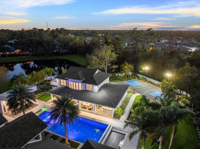 pool at dusk with a water view, a patio area, and basketball hoop