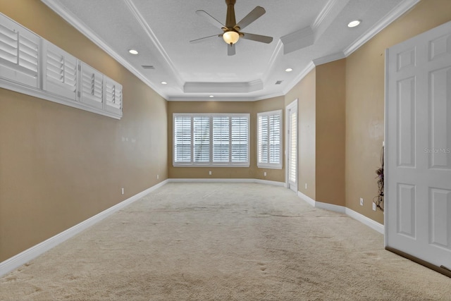 unfurnished room with ceiling fan, light colored carpet, a tray ceiling, and ornamental molding