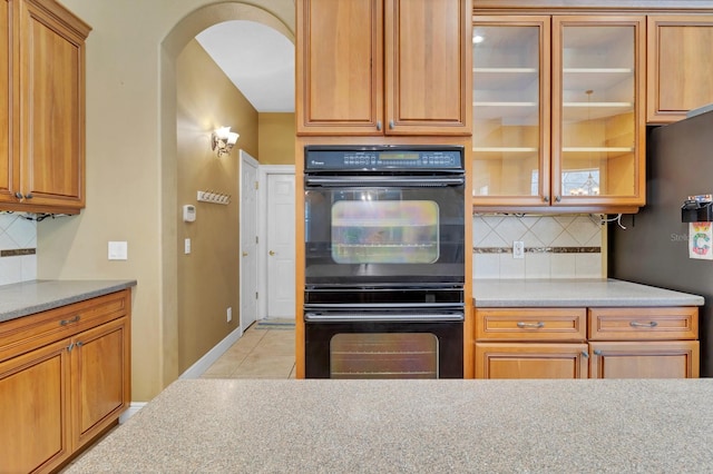 kitchen featuring black double oven, light stone counters, backsplash, and stainless steel fridge