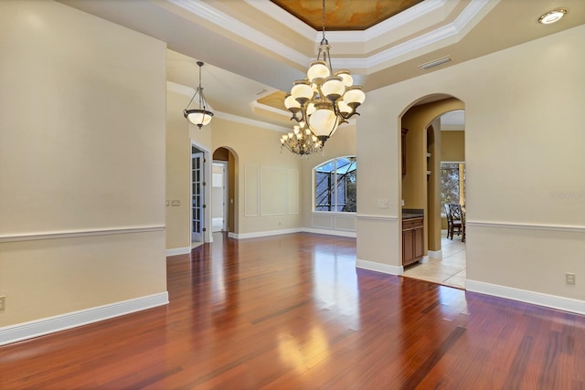 spare room with crown molding, a notable chandelier, a tray ceiling, and light hardwood / wood-style flooring