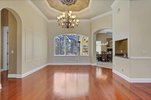 unfurnished dining area featuring crown molding, wood-type flooring, a tray ceiling, and a notable chandelier