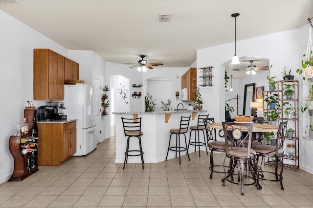 kitchen with light tile patterned floors, kitchen peninsula, white fridge with ice dispenser, light stone countertops, and pendant lighting