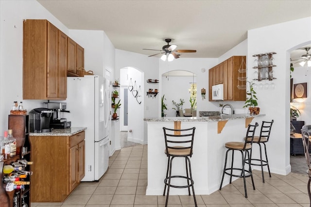 kitchen with light stone countertops, white appliances, ceiling fan, a breakfast bar, and light tile patterned floors