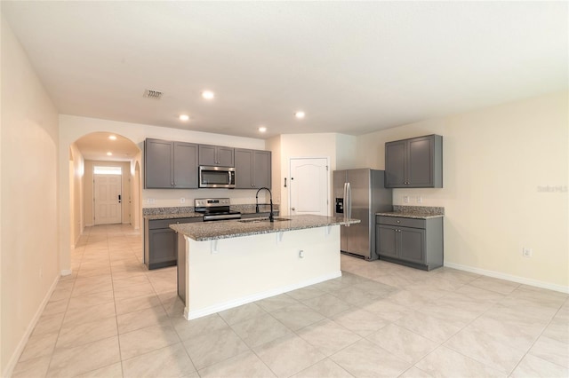 kitchen with gray cabinetry, stainless steel appliances, sink, a breakfast bar, and a center island with sink