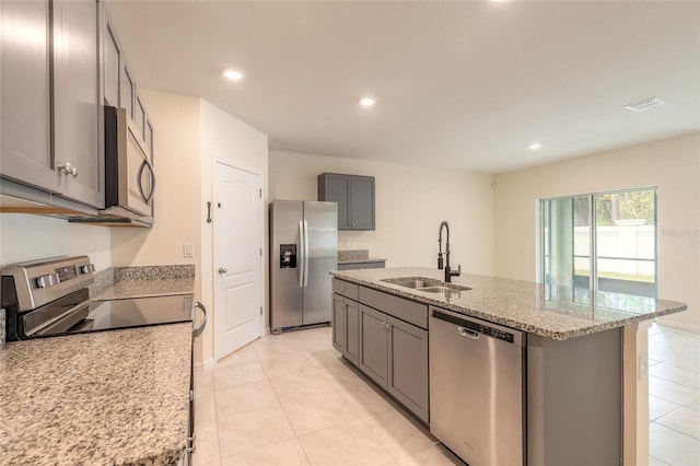 kitchen with appliances with stainless steel finishes, a center island with sink, light stone counters, and sink