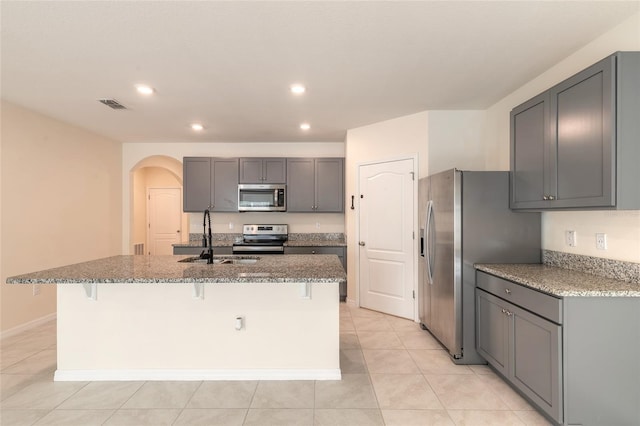 kitchen with a kitchen bar, a center island with sink, stainless steel appliances, gray cabinetry, and sink